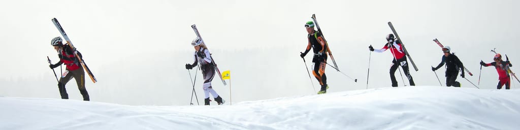 Eine Gruppe von Wintersportlern steigt mit geschulterten Skiern einen verschneiten Hang hinauf.